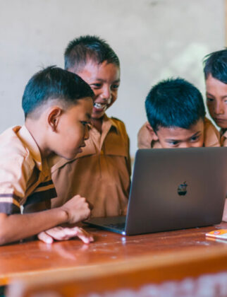 Group of children gathered around a laptop to learn, while having fun.